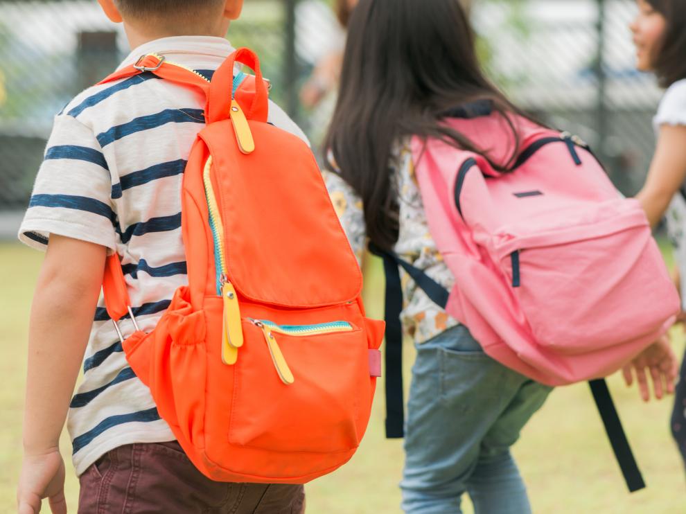 Three pupils of primary school go hand in hand. Boy and girl with school bags behind the back. Beginning of school lessons. Warm day of fall. Back to school. Little first graders.