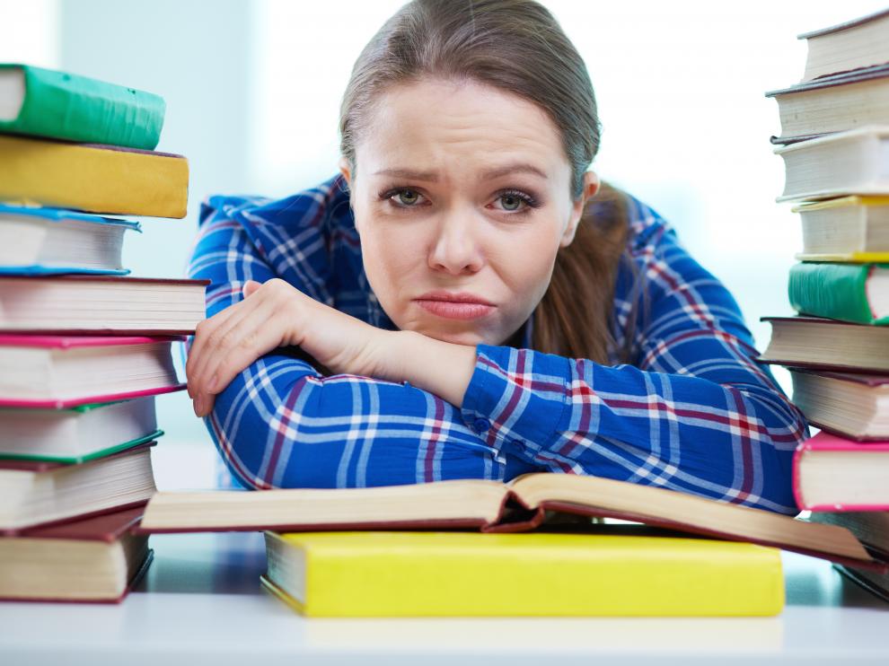Portrait of a frustrated student being surrounded with piles of books