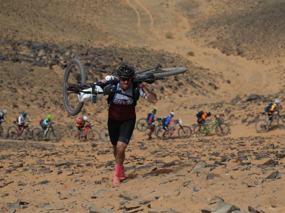 Un ciclista, con la bicicleta a hombros, sube una duna en la Titan Desert 2019.