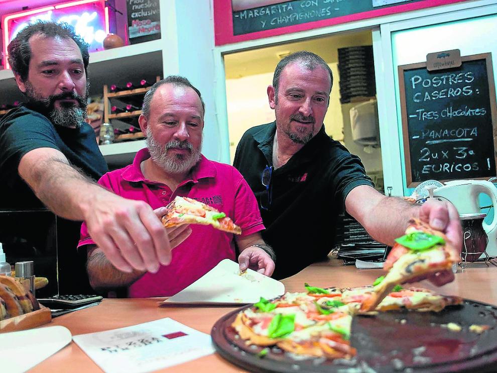 Hernán Romero, Javier Harguindeguy y Pablo Lozano cogiendo una pizza negra.