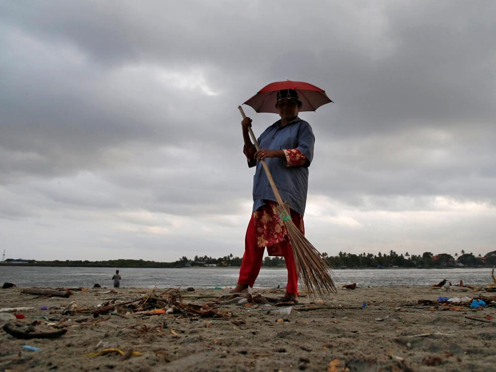 Un trabajador limpia una playa, con el telón de fondo de las nubes antes del monzón, en la playa de Fort Kochi en Kochi.