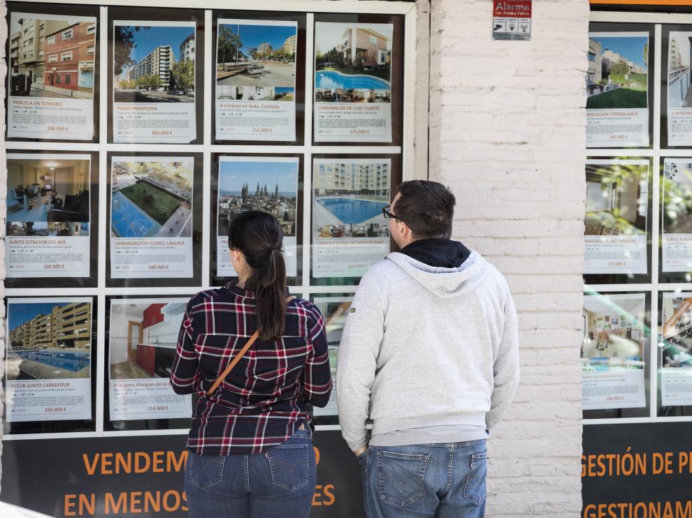 Una pareja mira anuncios de pisos en una inmobiliaria.