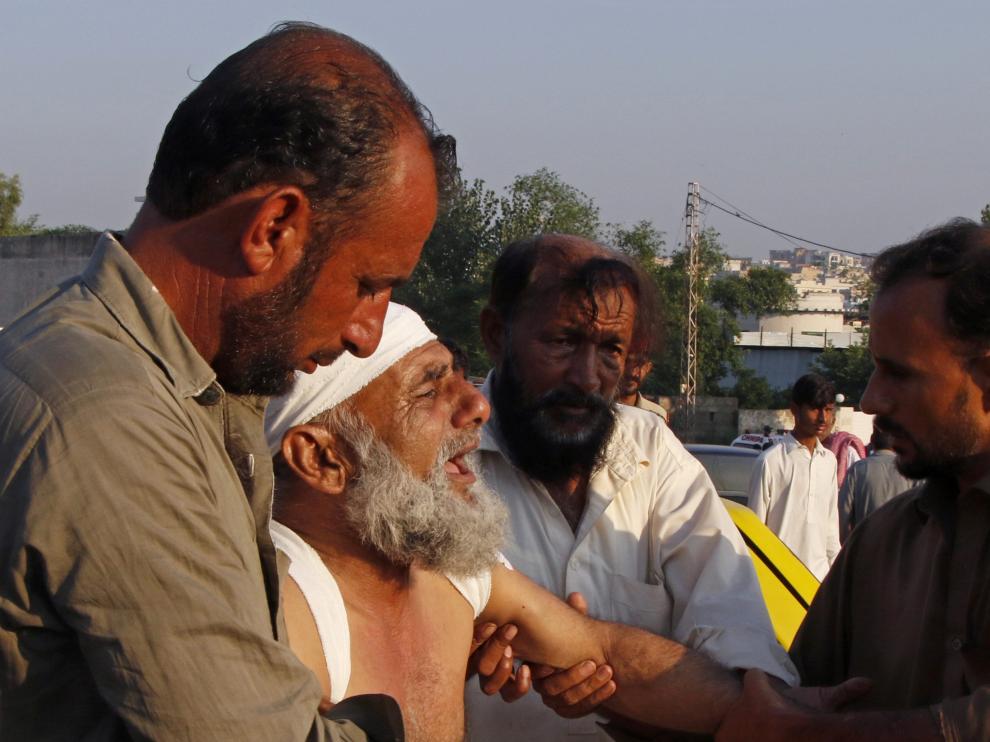 Varias personas ayudan a trasladar a un herido en el accidente áereo ocurrido en una zona de viviendas de Rawalpindi (Pakistán).