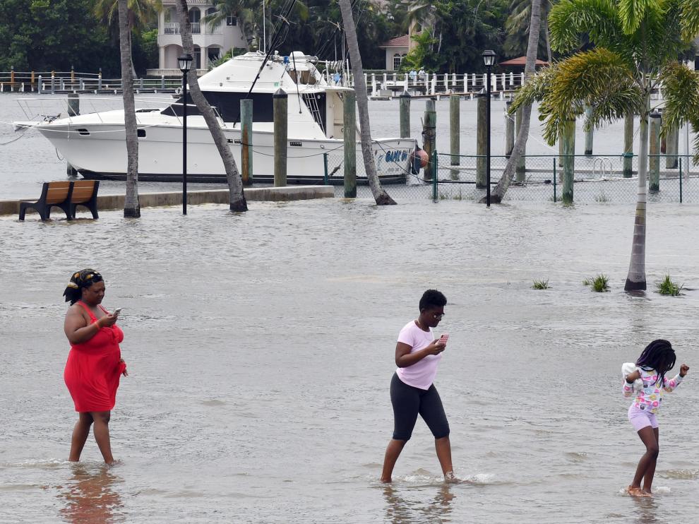 Un grupo de personas camina por una zona de parqueo inundada este lunes, ante la posible llegada del huracán Dorian, en Lantana, Florida.