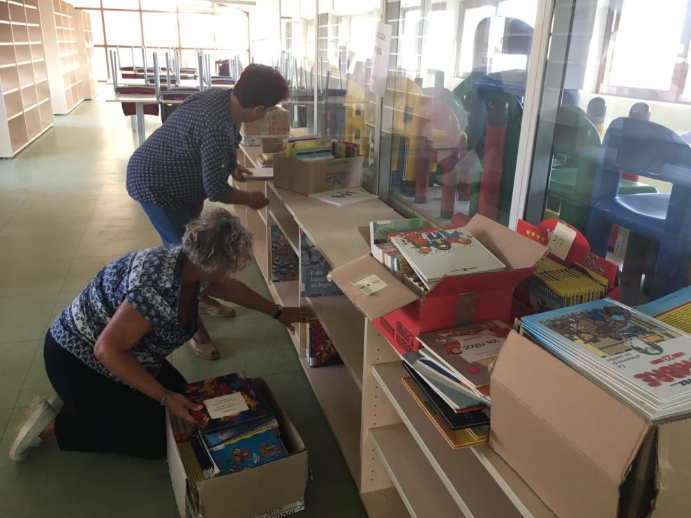 Dos voluntarias ordenan algunos de los libros infantiles en las nuevas instalaciones.