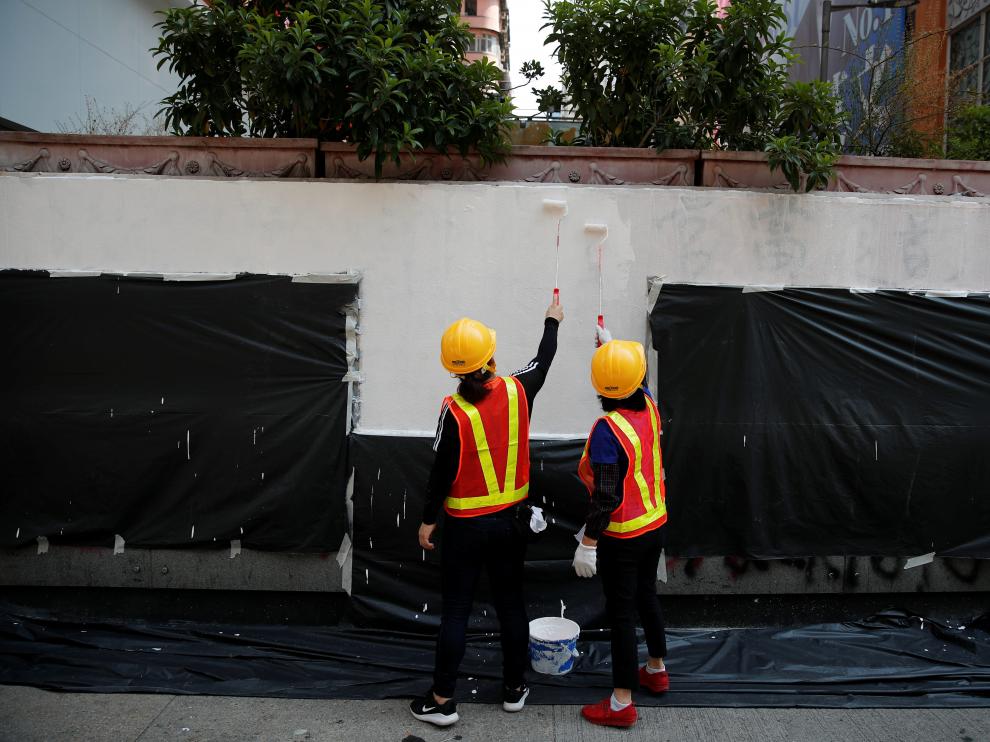 Dos trabajadores adecentan una fachada con pintadas tras una manifestación en Hong Kong