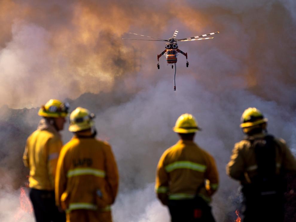 Varios bomberos miran cómo un helicóptero arroja agua sobre el incendio Getty.