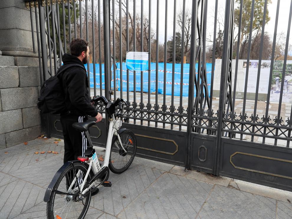 Un joven lee el cartel instalado por el Ayuntamiento en uno de los accesos de El Retiro, que permanece cerrado al público este domingo.
