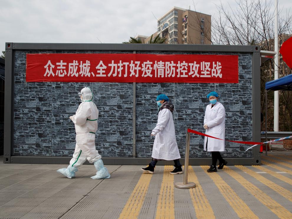 Personal de un hospital con ropa protectora camina hacia un punto de control en la zona de exclusión de la provincia china de Hubei