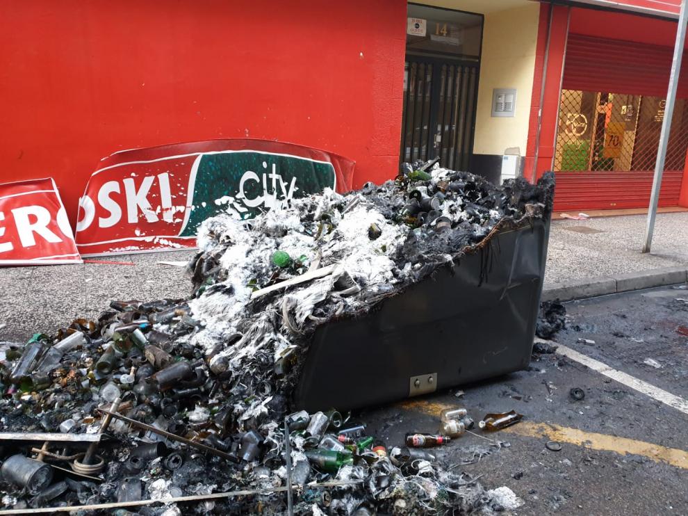 Los restos de los contenedores quemados este domingo por la mañana. El fuego ha afectado a la fachada de un supermercado, dos motos y una vivienda.