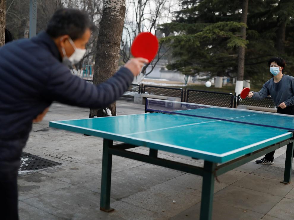 Dos personas con mascarilla juegan al tenis de mesa en un parque de Pekín
