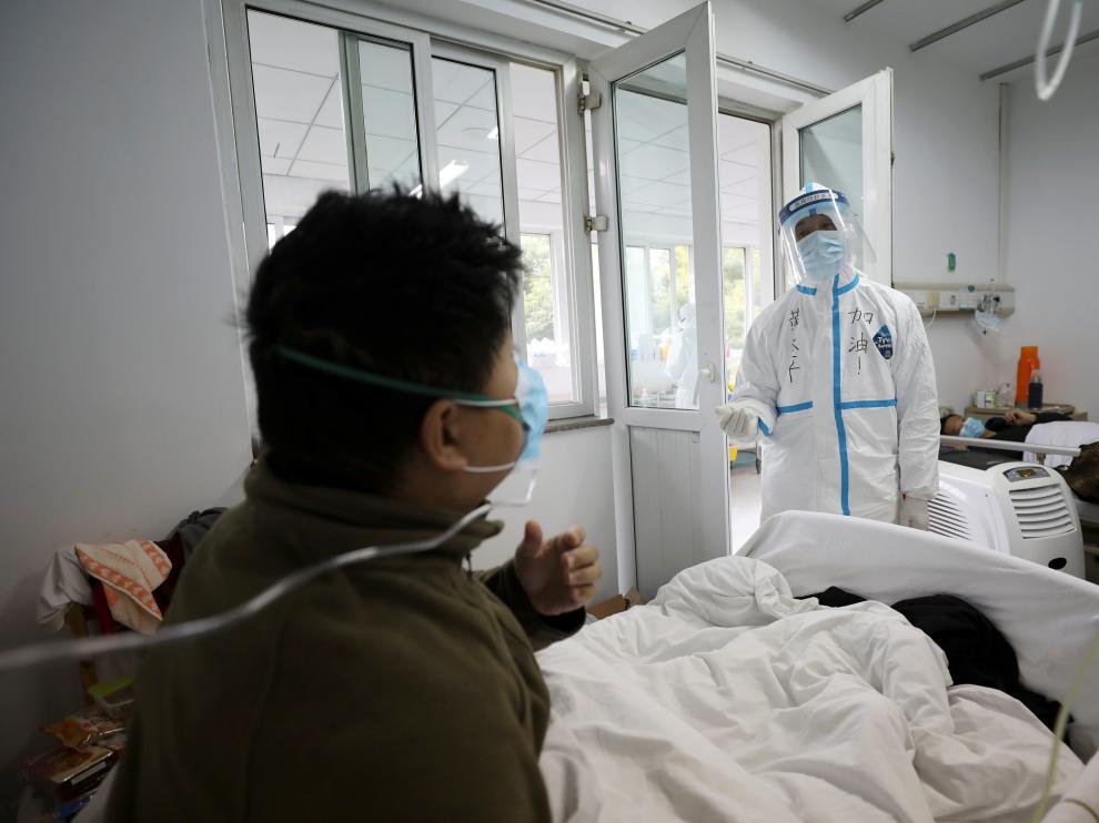 Un profesional sanitario con el traje de seguridad interactúa con un paciente en una habitación de aislamiento de un hospital en Wuhan.