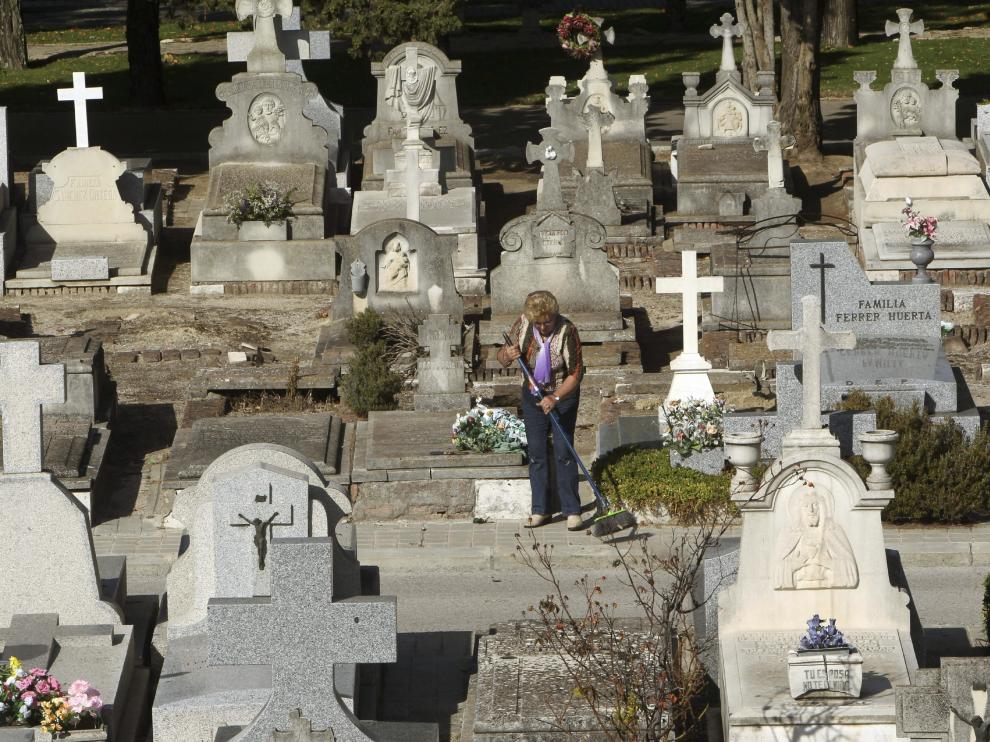 Una mujer limpia la lápida de una tumba en el cementerio de La Almudena.