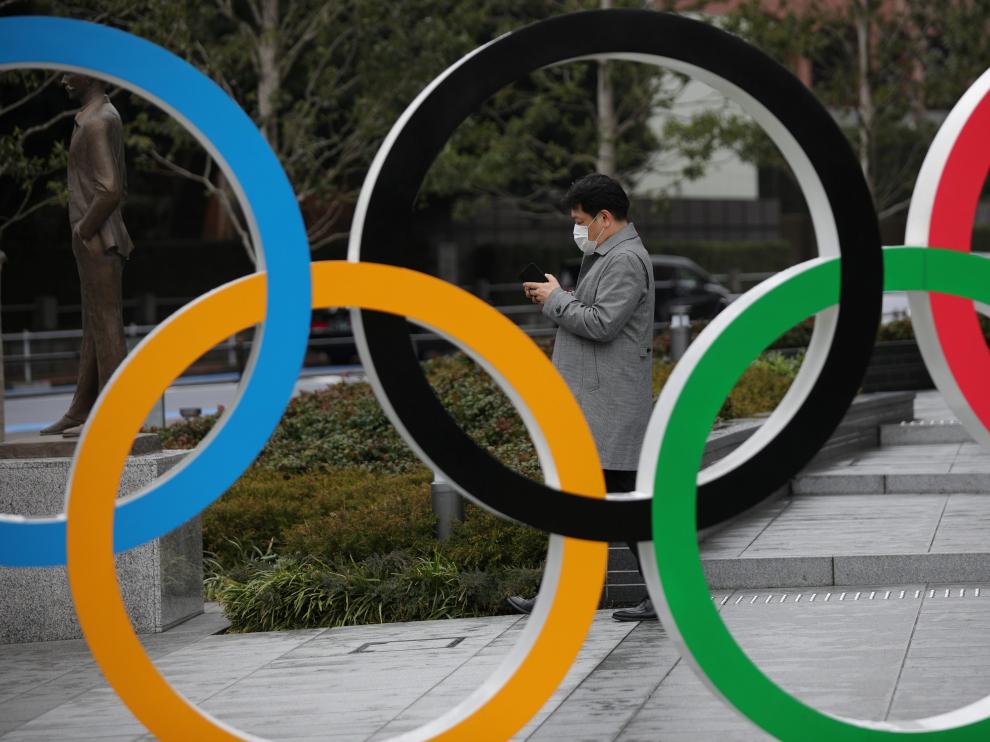 Man wearing protective face mask looks at his mobile phone next to The Olympic rings in front of the Japan Olympics Museum in Tokyo