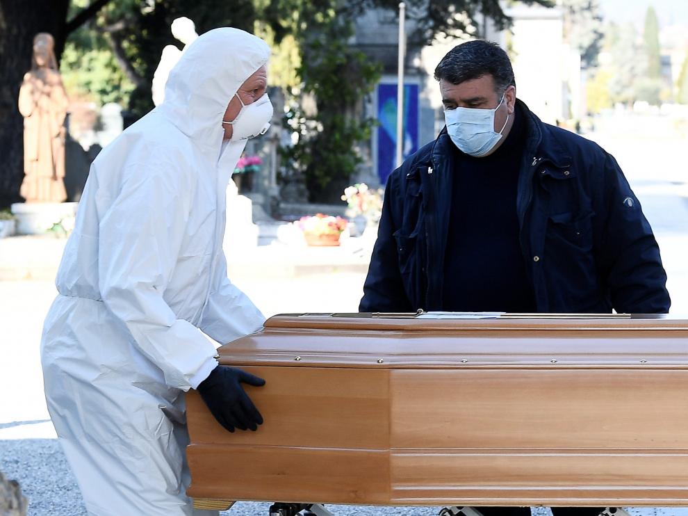 Dos personas con protección trasladan a una persona fallecida por coronavirus en Bérgamo.
