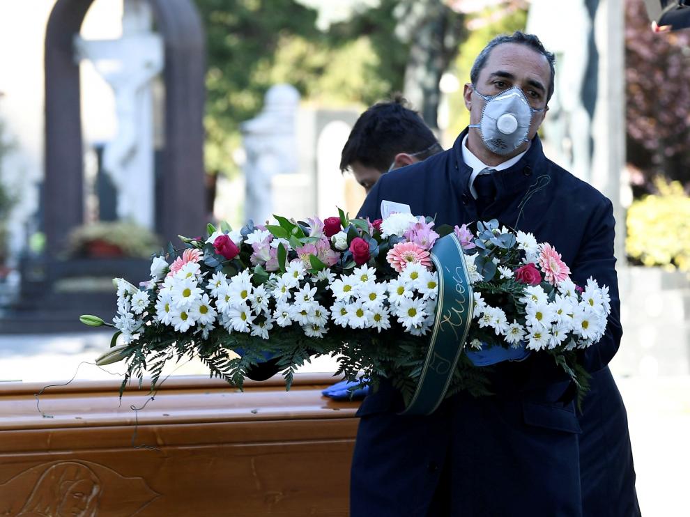 Un trabajador de una funeraria transporta una corona de flores en un cementerio de Bérgamo, en Italia.