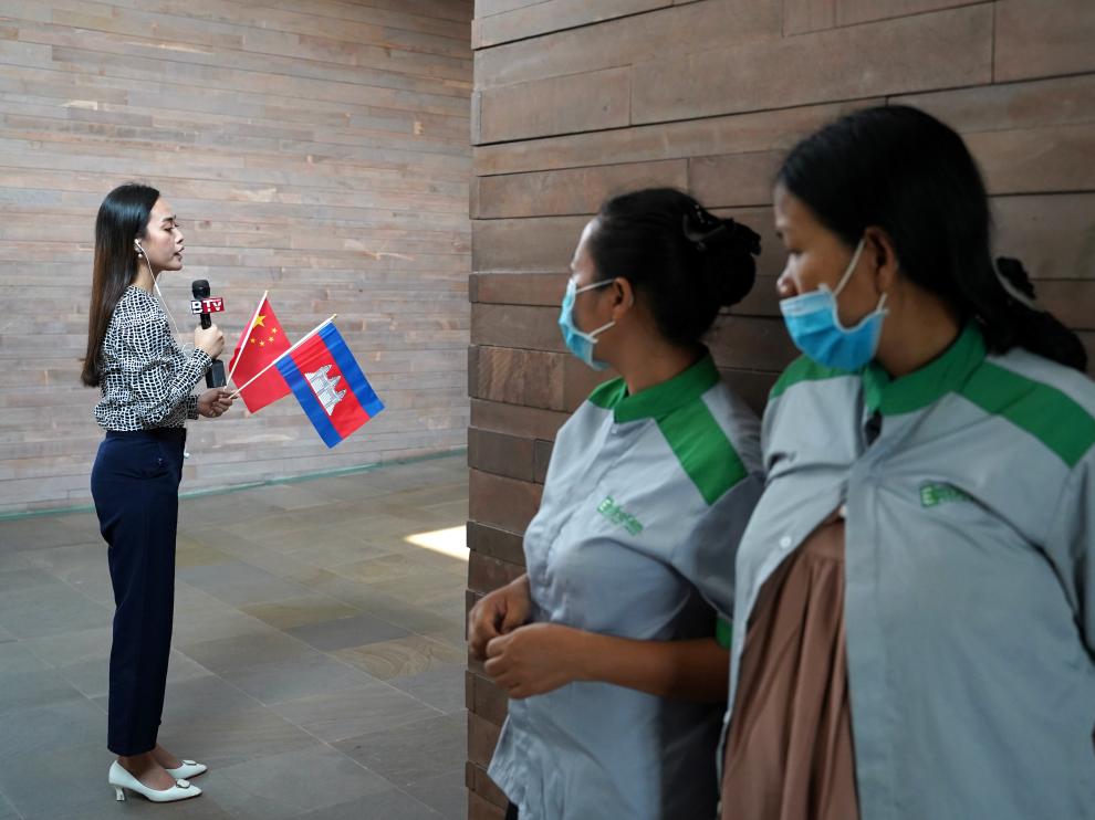 Airport cleaners in face masks observe a Cambodian TV reporter as a plane arrives from China to Cambodia with supplies and doctors donated to contain the spread of the coronavirus disease (COVID-19) outbreak