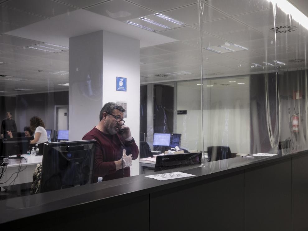 Un funcionario, atendiendo el teléfono detrás del mostrador del juzgado de guardia de Zaragoza, protegido con una cortina de plástico.