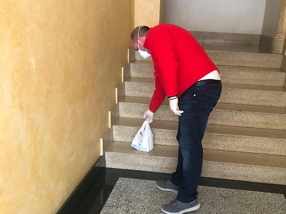 Un voluntario deposita una bolsa de medicamentos en las escaleras de acceso a una vivienda