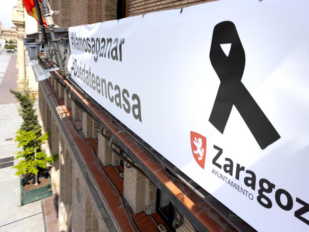 pancarta colgada en el balcón municipal, a la que se ha añadido el crespón negro en recuerdo y homenaje de las víctimas del COVID-19 y sus familias.