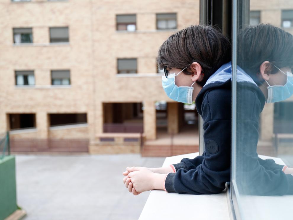 Un niño se asoma a la ventana con mascarilla, en una población de Madrid.