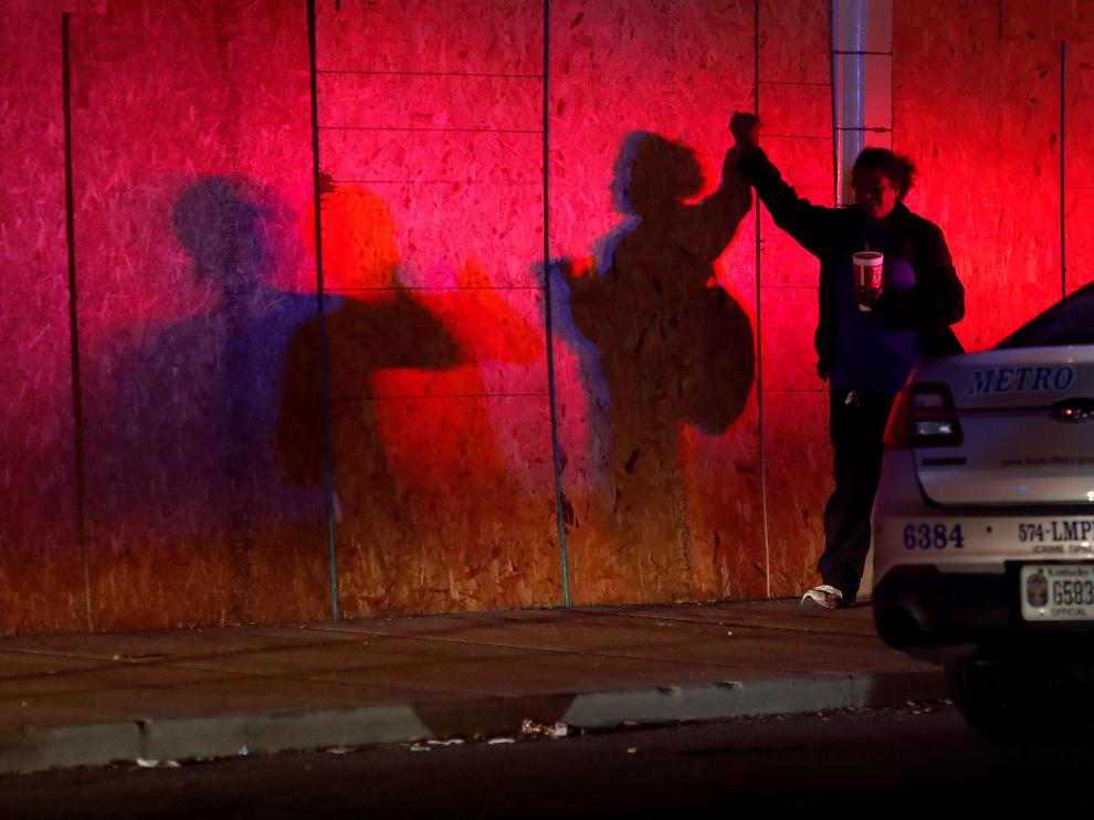 A woman stands by a police vehicle before a 9pm curfew in Louisville, Kentucky