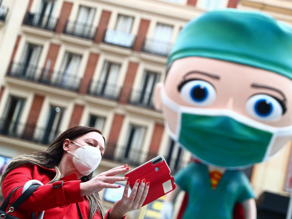 A woman wearing a protective face mask takes a selfie next to an oversized model of a health worker in Madrid