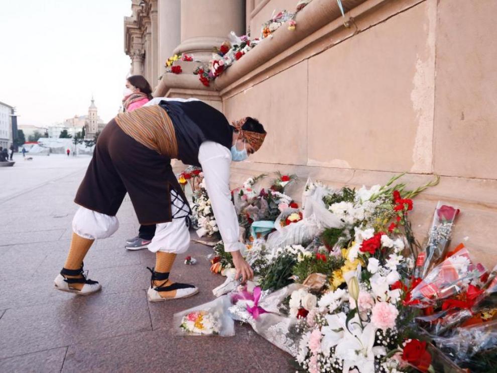Un hombre vestido con el traje regional aragonés deposita un ramo de flores en la plaza del Pilar.