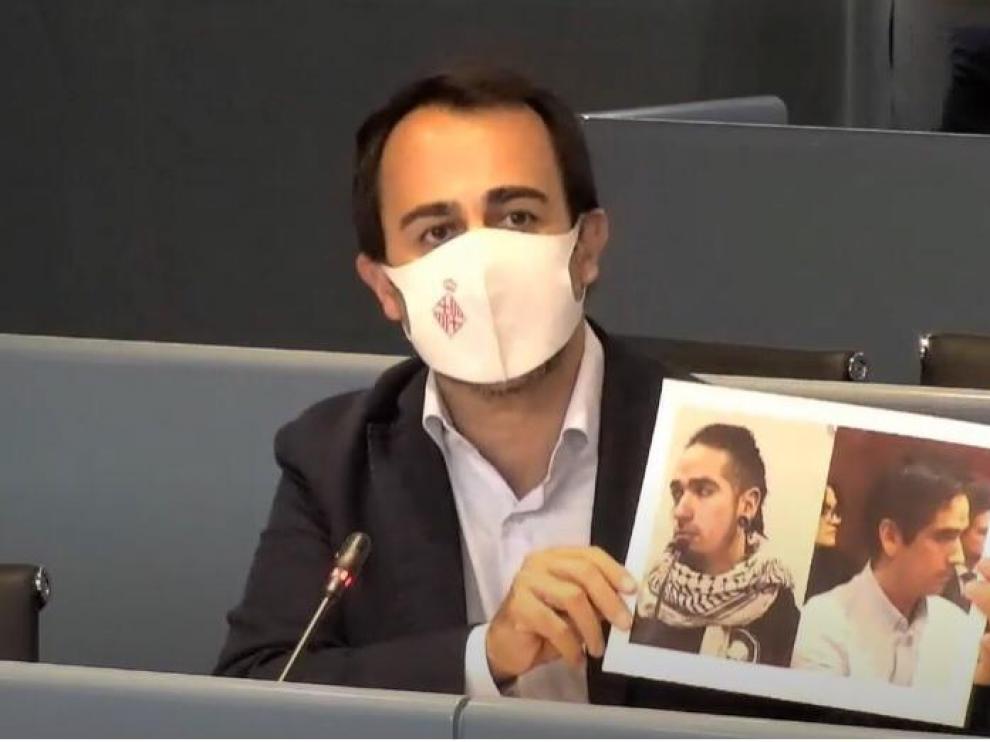Óscar Ramírez, concejal del PP, muestra dos fotos de Rodrigo Lanza al realizar su propuesta de retirar el premio Ciudad de Barcelona al documental sobre su historia.