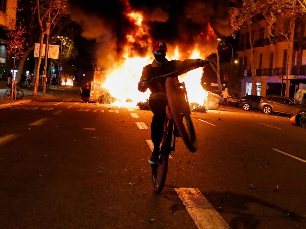 Un joven con una moto pasa junto a una barricada ardiendo en Barcelona