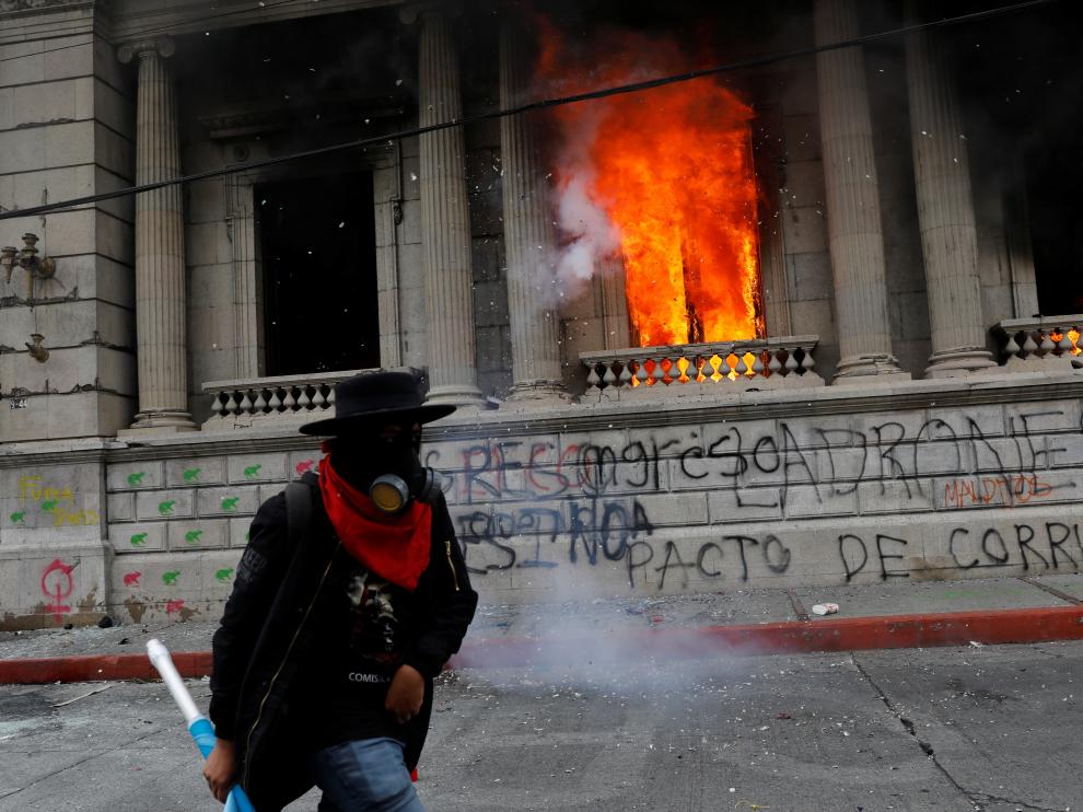 Un hombre que participaba en las protestas camina junto al Congreso guatemalteco en llamas.