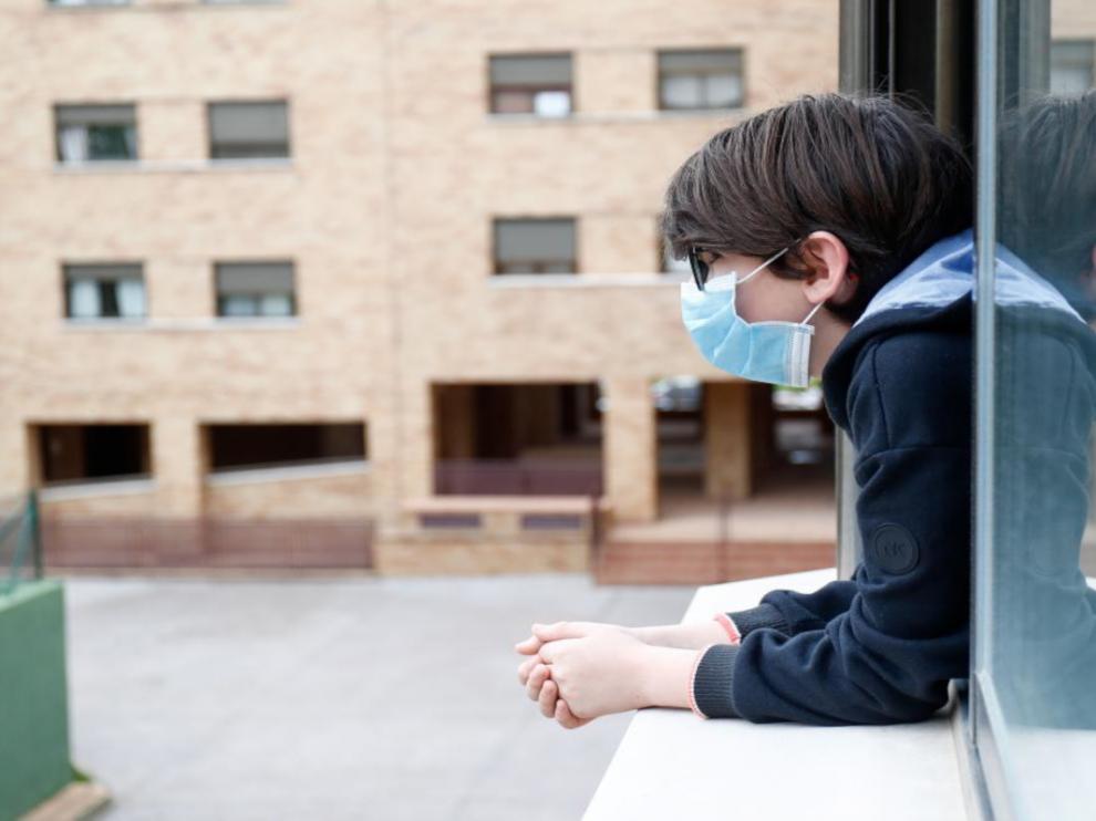 Un niño se asoma a la ventana con mascarilla, en una población de Madrid.