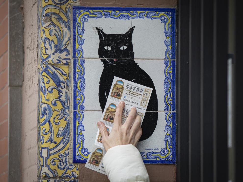 Una persona pasa varios décimos de lotería de Navidad por el azulejo de una administración en Sevilla.