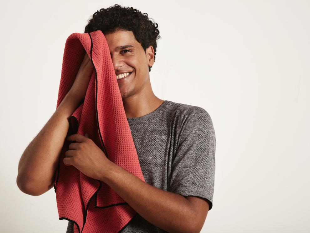 Young attractive black sportsman laughs and wipes his face with a red towel, right half of the face open, against white background