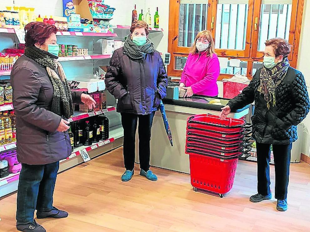 Inma Hueso, tras el mostrador, atiende y charla con tres vecinas de la localidad zaragozana de Malón