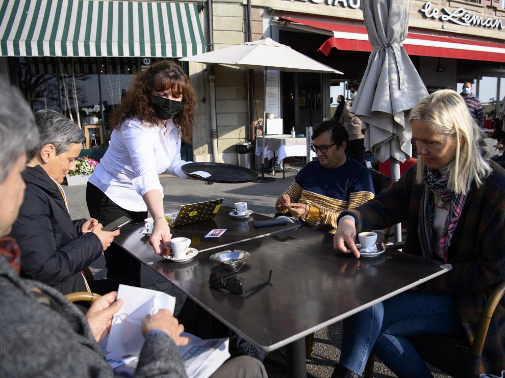 Un camarero con mascarilla sirve cafés a varios clientes en la terraza de un restaurante de Nyon. En Suiza los interiores de los bares siguen cerrados.