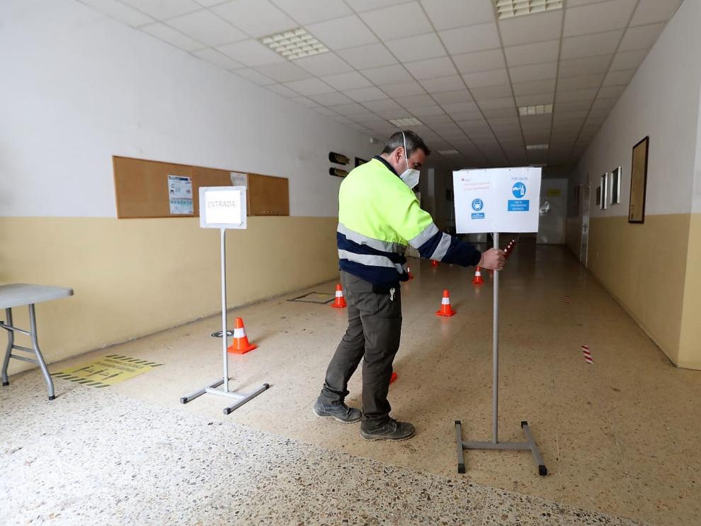 Un empleado de las brigadas municipales coloca los carteles de acceso a la sala de vacunación en el local vecinal.