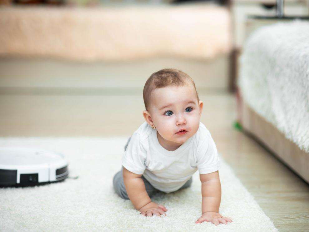Robotic vacuum cleaner on the carpet, next to the baby girl
