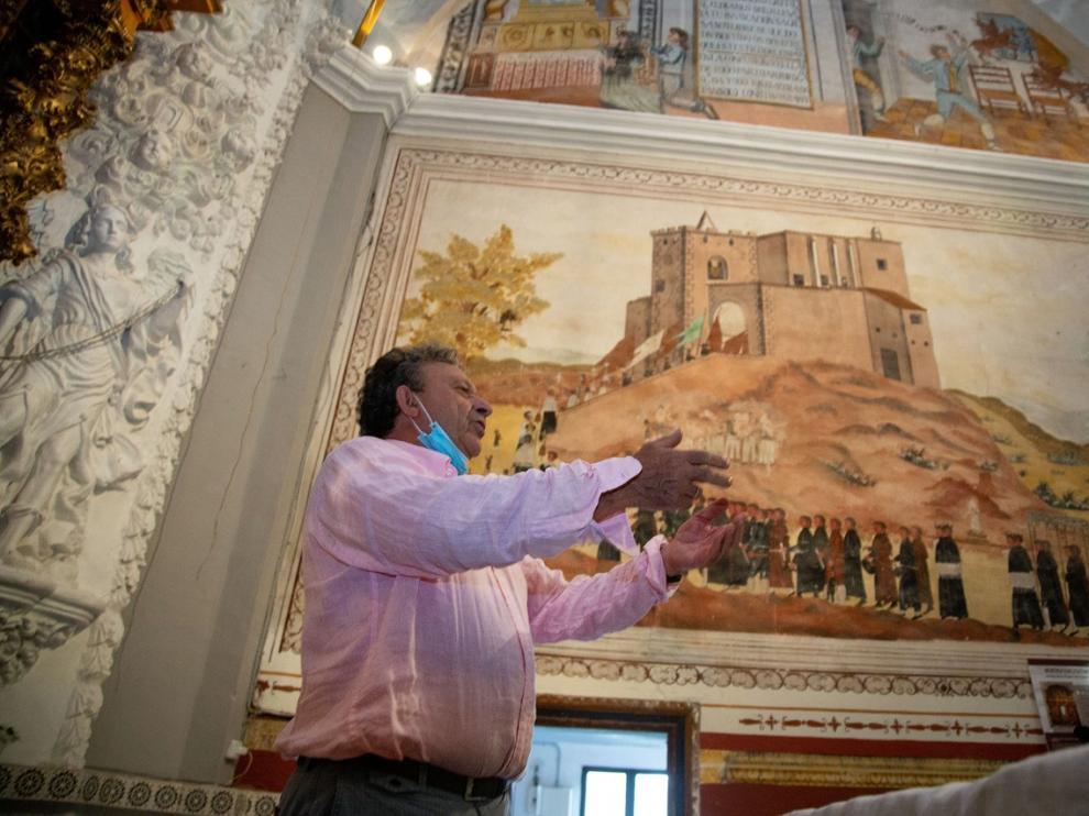 El alcalde de Bijuesca explica cómo es la romería de la Saca de la Virgen ante una pìntura de la ermita que la reproduce
