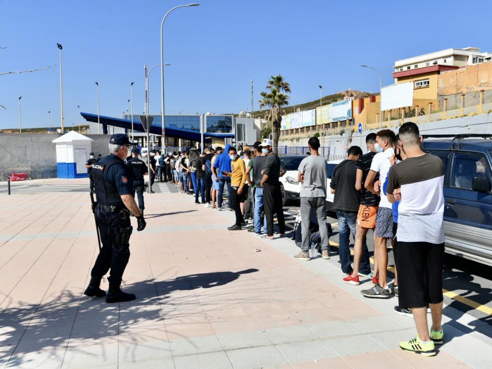 Varios migrantes procedentes de Marruecos hacen cola en las puertas de la frontera de Ceuta donde agentes de la Policía Nacional reparten citas para solicitud de asilo.