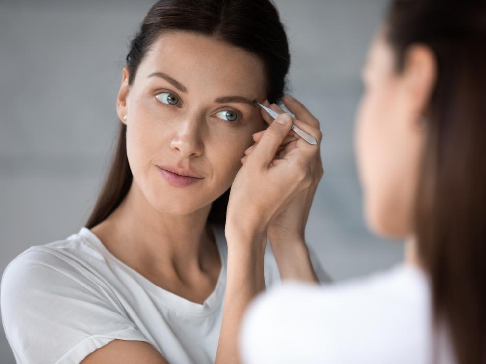 Una mujer retoca sus cejas con pinzas para un estilismo perfecto