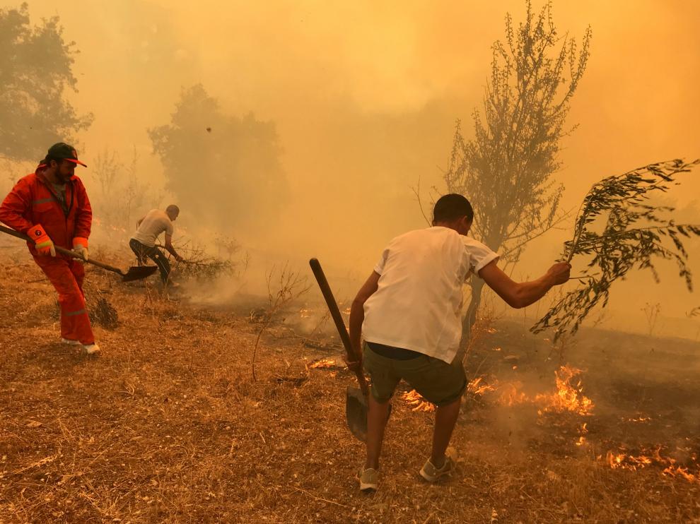 People use tree branches in an attempt to put out the flames of a wildfire in Iboudraren village