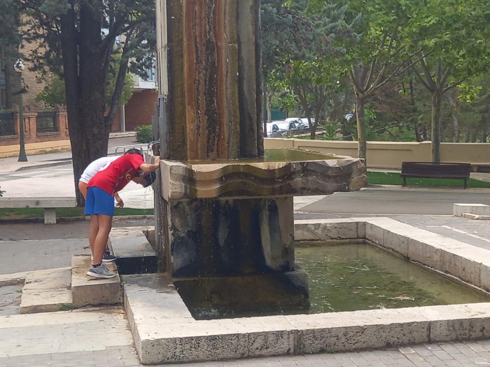 Dos chicos se refrescan en plena ola de calor en la fuente de Torán de Teruel.