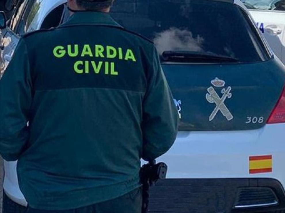 Un agente de la Guardia Civil de espaldas y junto a un vehículo oficial del cuerpo.