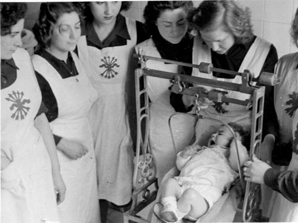Jóvenes zaragozanas pesan a un bebé durante las prácticas del Servicio Social en 1944.