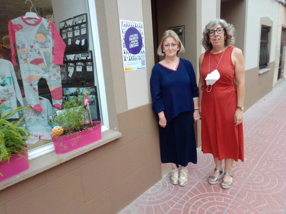 María Luisa Roche y Paca Miguel, comerciantes de La Puebla de Alfindén, junto a un cartel en un comercio.