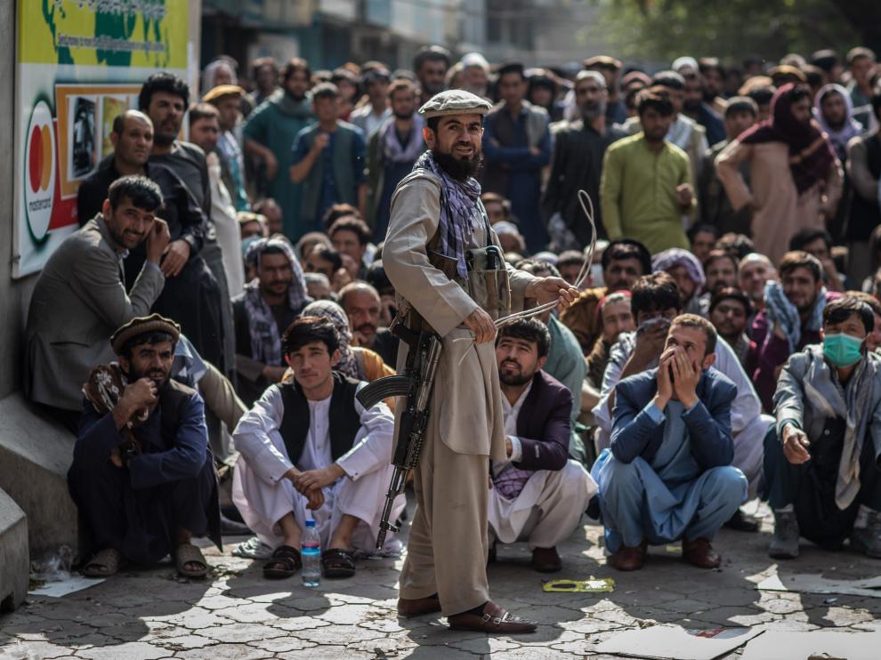 Un talibán, delante de un grupo de hombres que esperan que abra un banco para sacar dinero, en Kabul