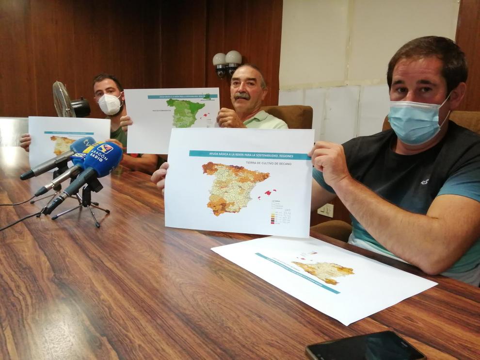 De izquierda a derecha, César Izquierdo, Ricardo Plumed y Francisco Ramo, de la plataforma Agrigate, muestran el mapa de reparto de ayudas. En color claro, las provincias cuyos agricultores percibirán menos dinero.