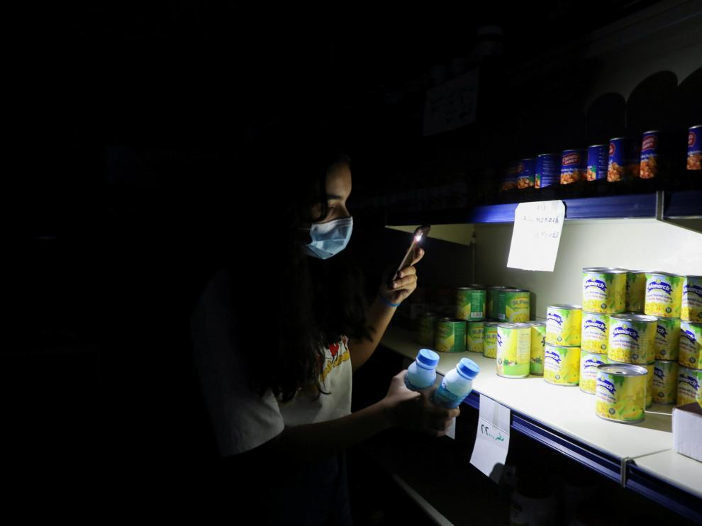 Una joven compra en un supermercado ayudada por la linterna de su móvil