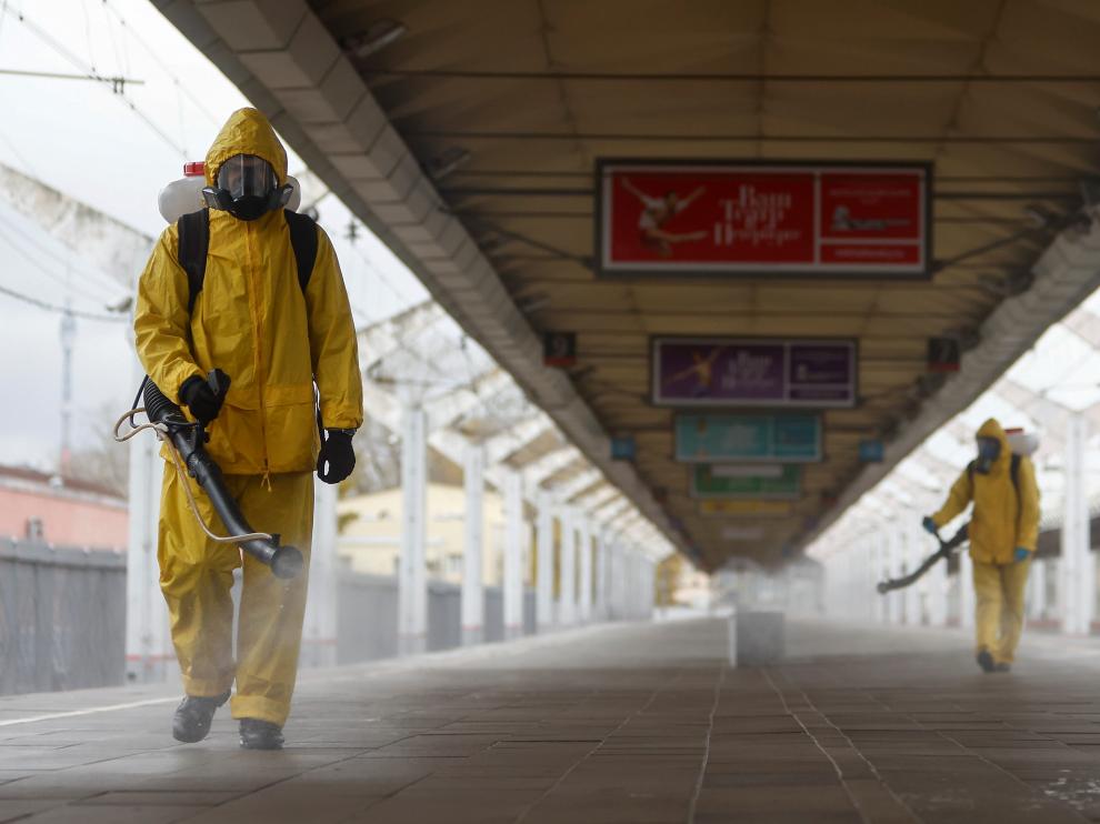 Dos operarios con trajes de protección desinfectan una estación de tren en Moscú